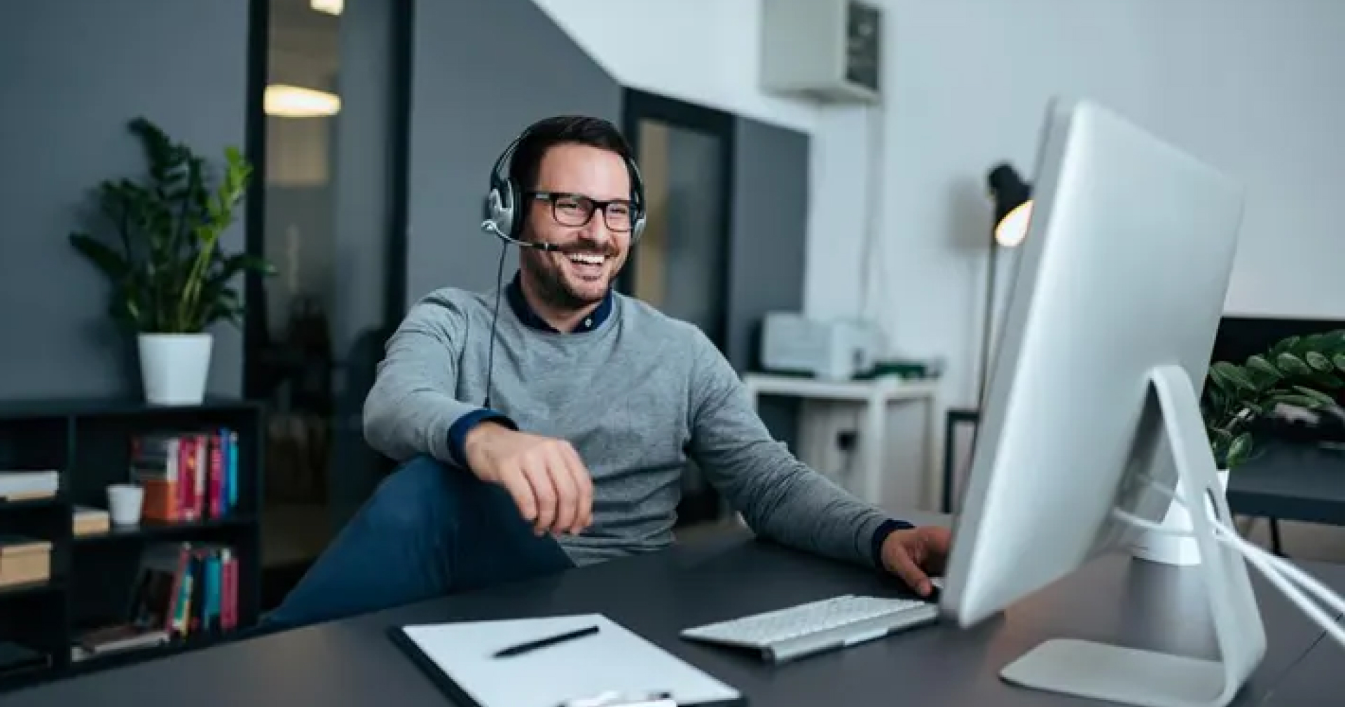 Male customer service representative smiling at desk talking a to happy client